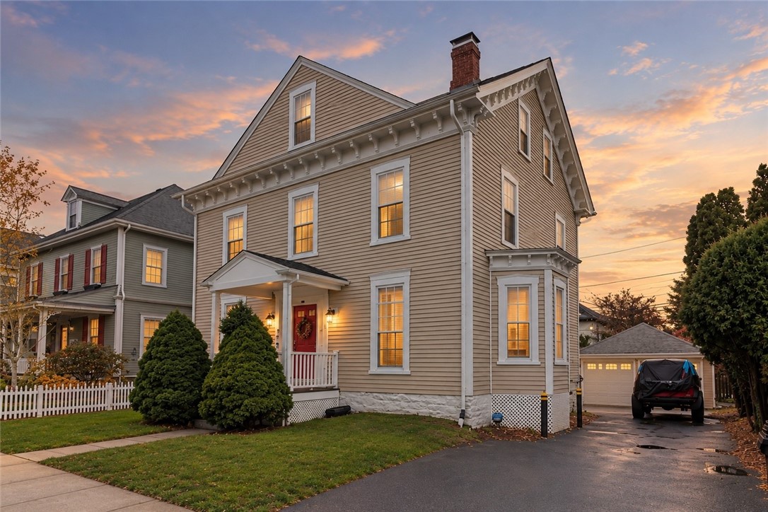 Two-story taupe clapboard house with a red front door, photographed at sunset.