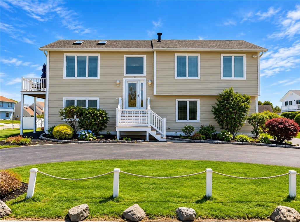 Beige two-story home with white entry stairs, landscaped shrubs, and a small side deck.