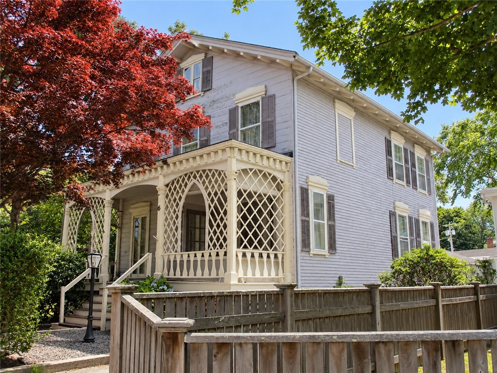 Two-story white house with a lattice-covered porch, wooden fence, and mature trees.