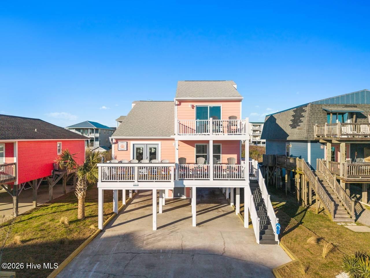 Elevated view of a peach coastal home with two white-railed decks and neighboring beach houses.