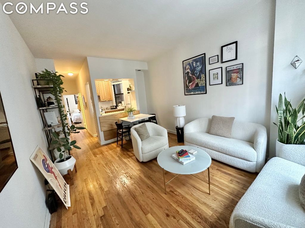 Furnished apartment living room with white seating, hardwood floors, and an open view to the kitchen.
