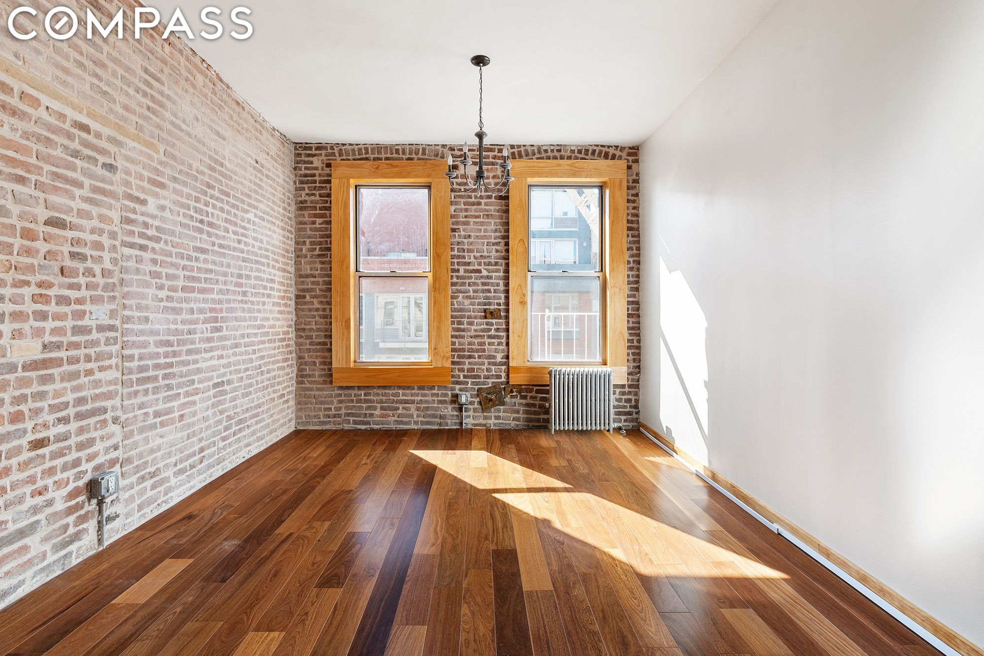 Empty room with exposed brick walls, hardwood floors, and two wood-trimmed windows.