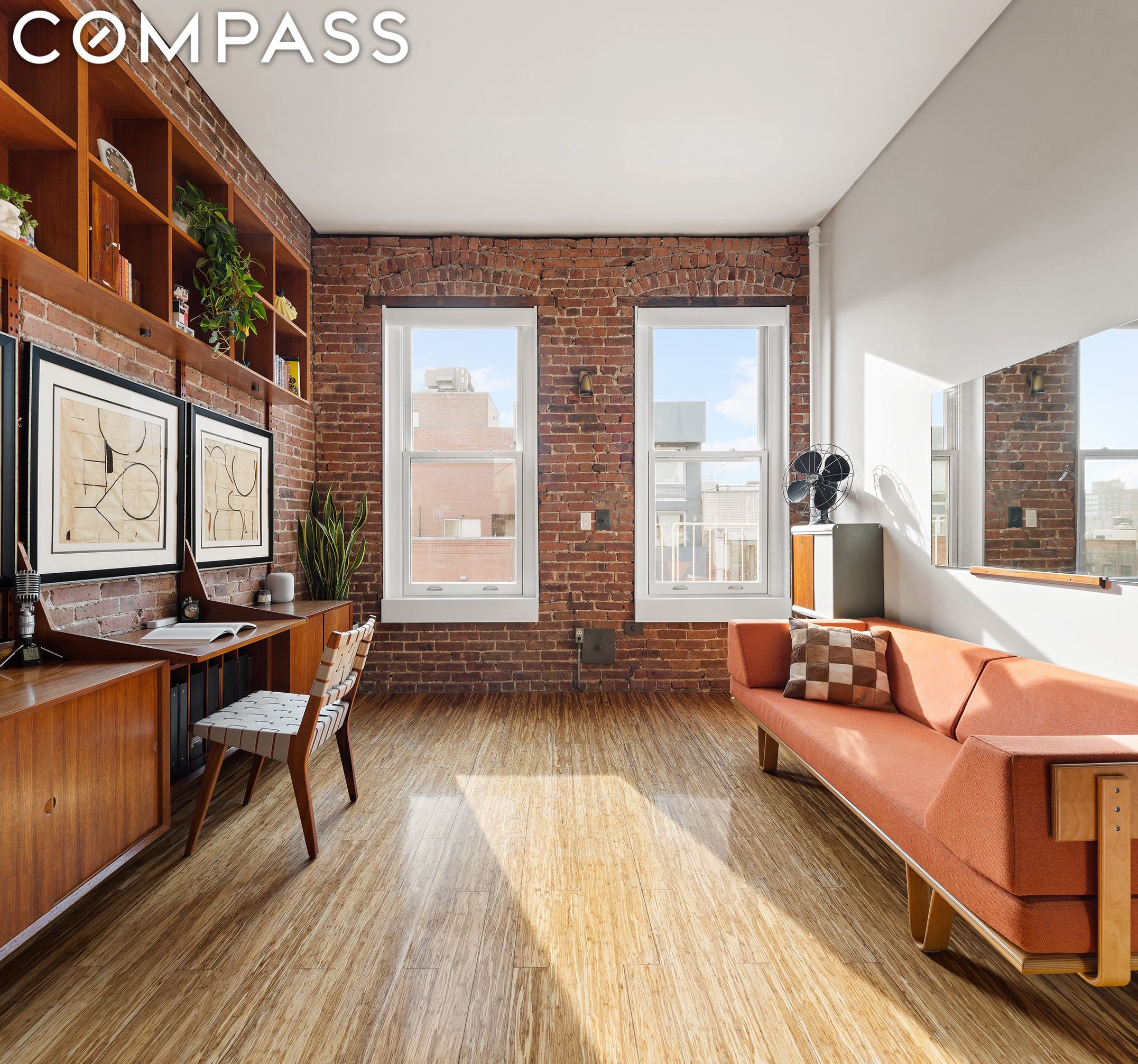 Living room with exposed brick walls, built-in shelving, two tall windows, and a coral sofa.
