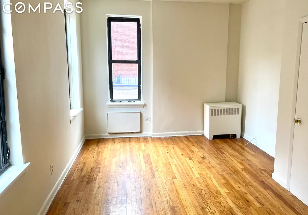 Unfurnished room with hardwood floors, two windows, and a wall radiator.