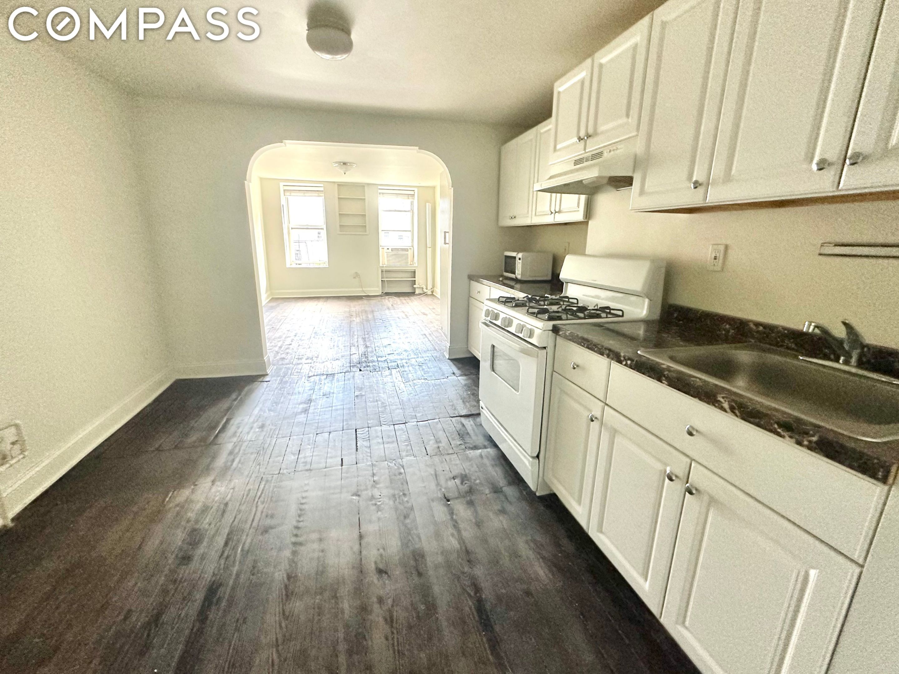 Kitchen with white cabinets and a gas range opening to a bright room through an archway.