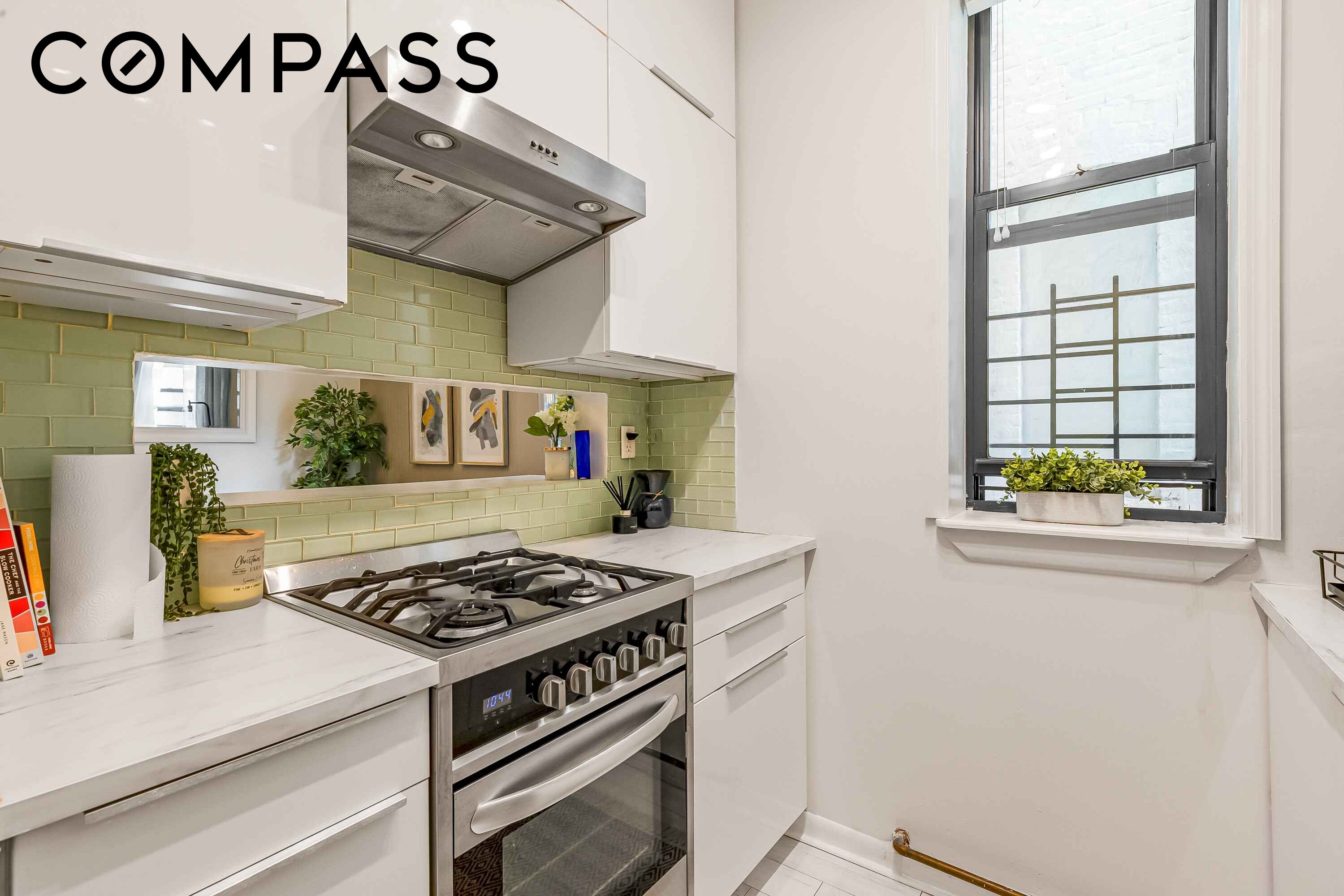 Renovated kitchen with a stainless steel gas range, green tile backsplash, and large window.