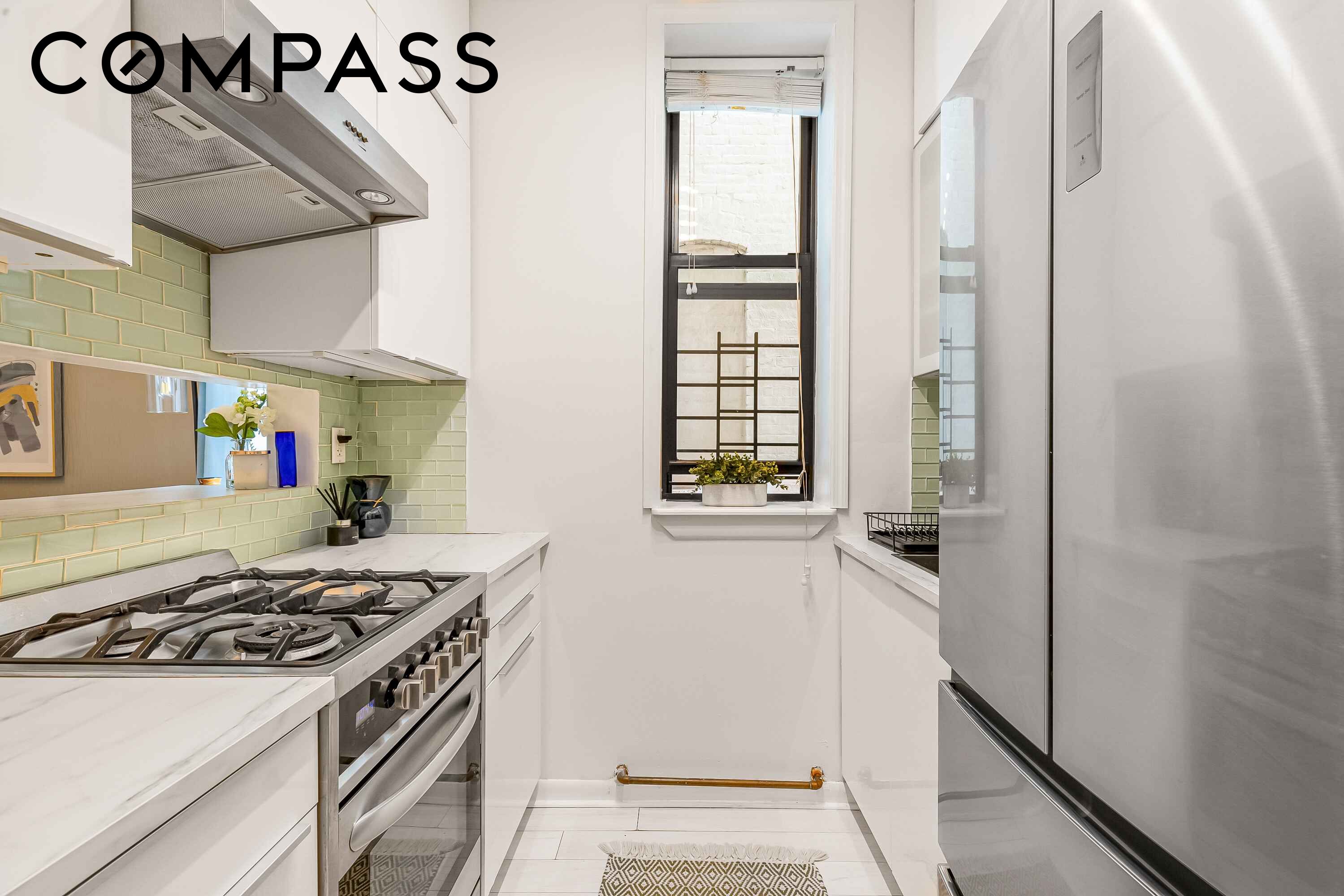 Galley kitchen with pale green tile, stainless-steel appliances, and a tall window.