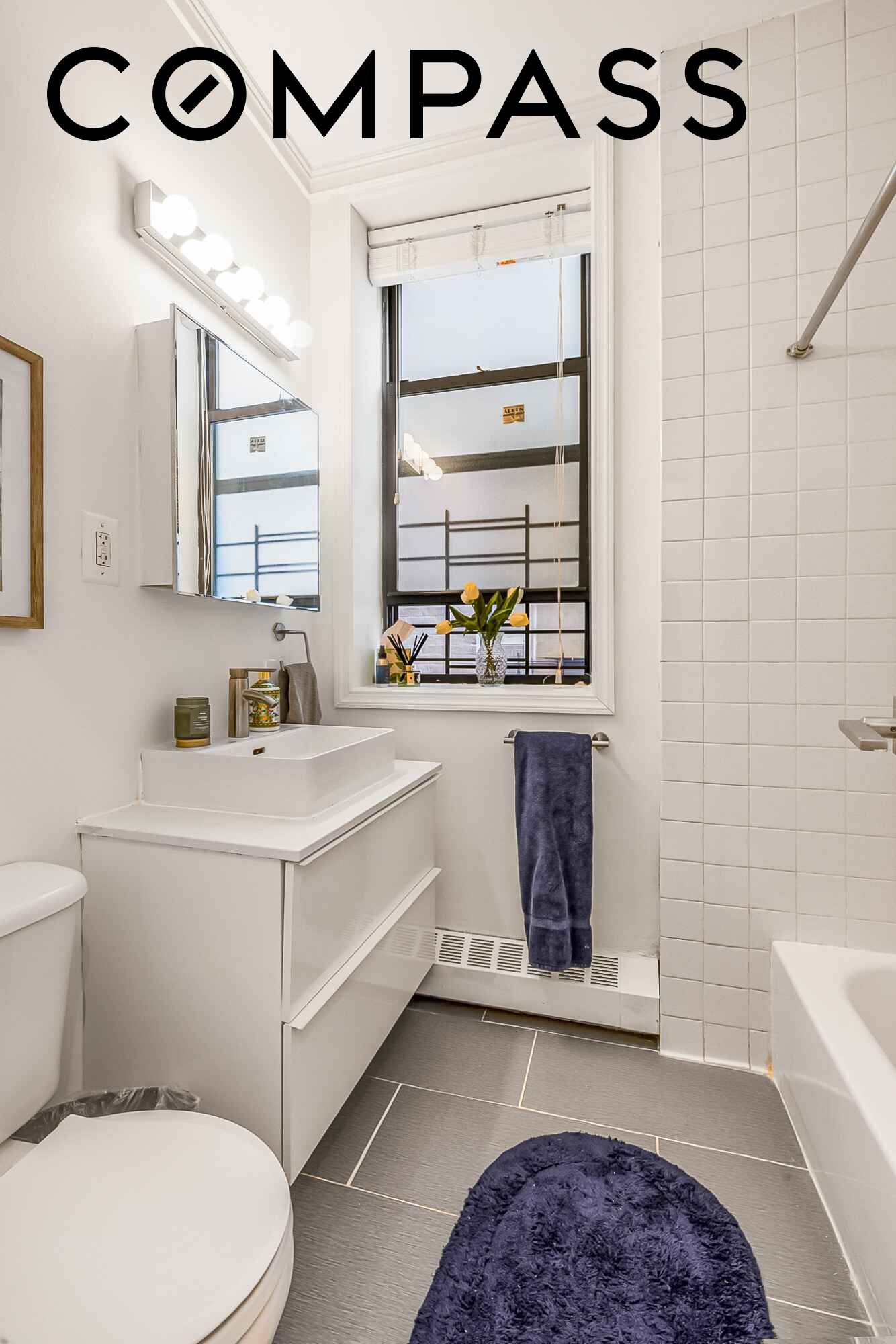 Bright bathroom with a white vessel-sink vanity, large window, tiled tub surround, and navy accents.