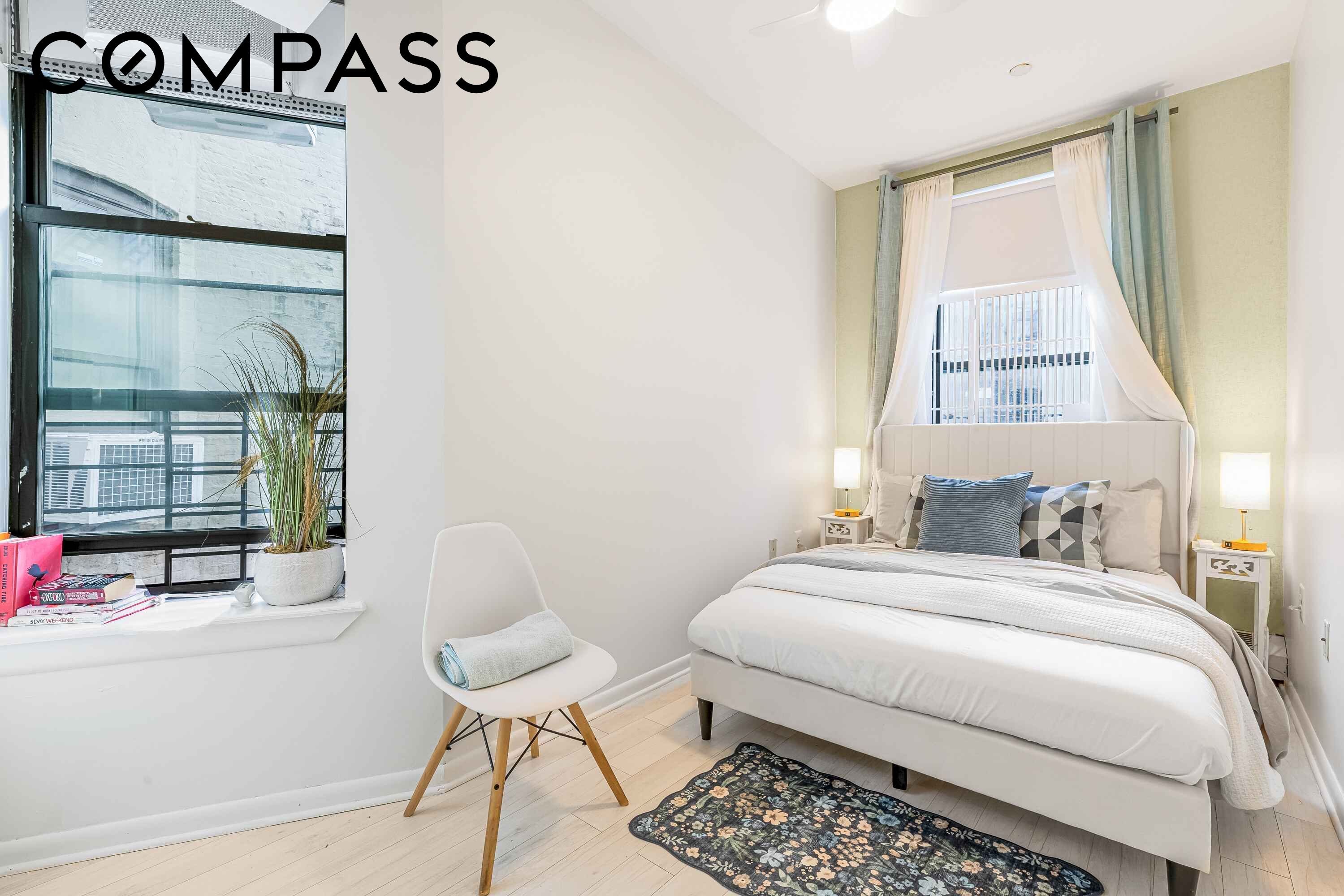 Furnished bedroom with a white bed beneath a curtained window and a floral rug.