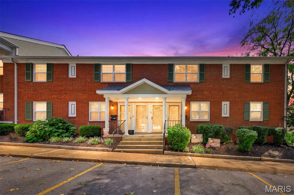 Two-story brick residential building with a columned entry, green shutters, and parking in front.