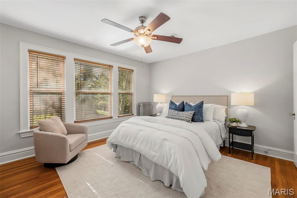 Staged bedroom with a white bed, blue pillows, three windows, and hardwood floors.