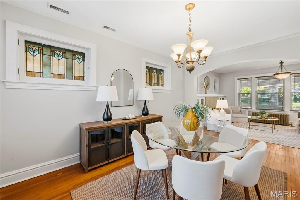 Dining room with stained-glass windows, a glass-top table, white chairs, and a chandelier.