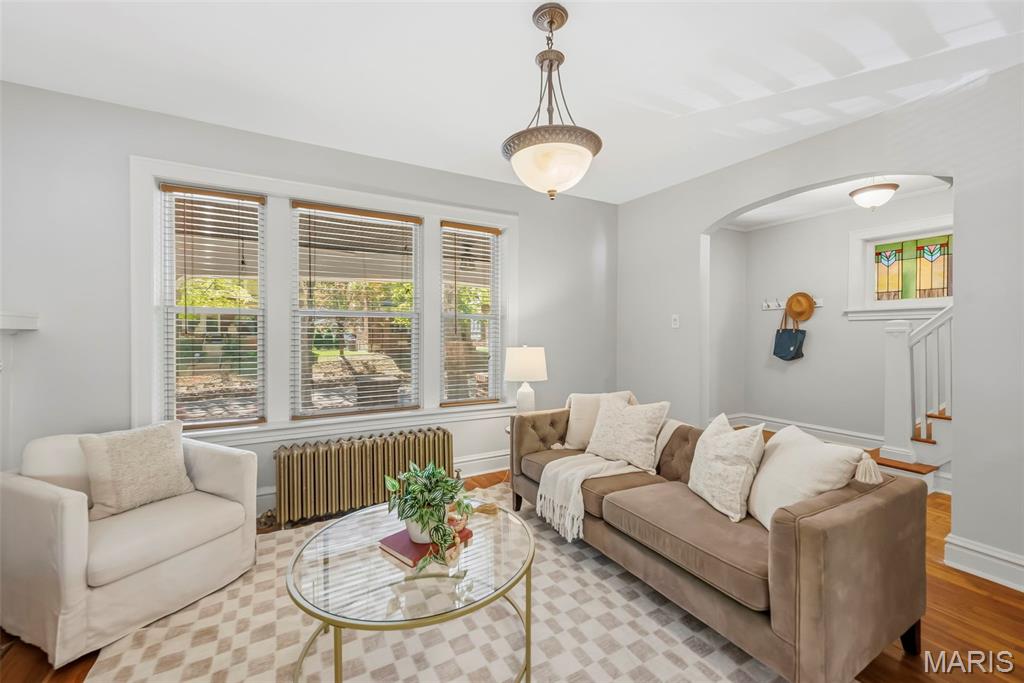 Living room with a taupe sofa, white armchair, three front windows, and an arched opening to the staircase.