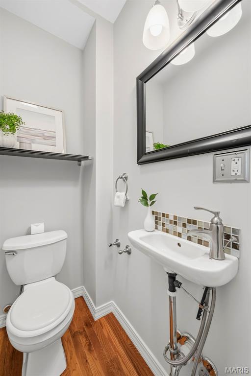 Bathroom with a pedestal sink, toilet, black-framed mirror, and wood flooring.