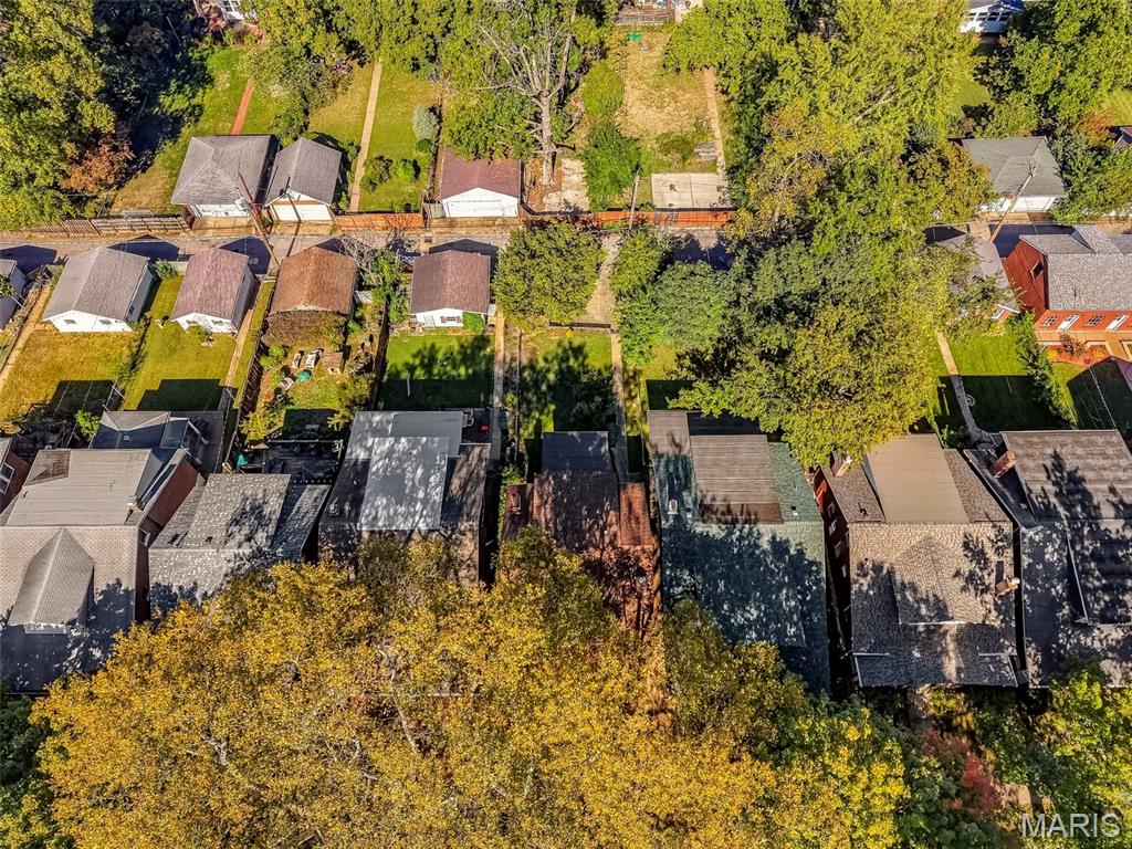 Aerial view of homes and fenced backyards beneath mature autumn trees.
