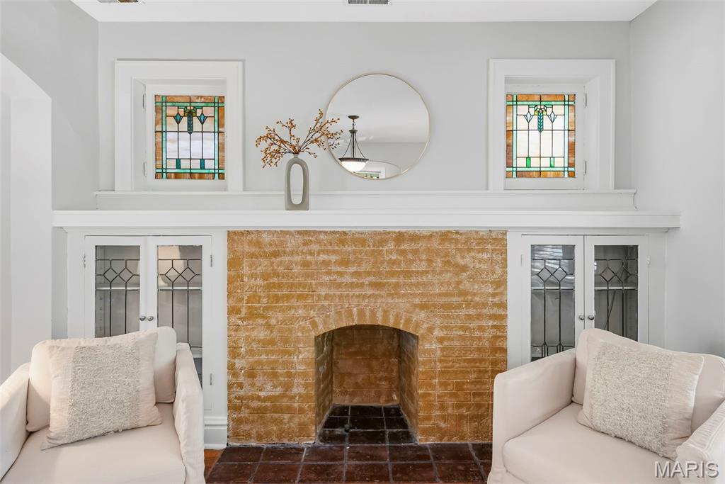 Living room fireplace with orange brick, stained-glass windows, and white armchairs.