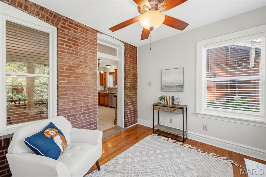 Living room with exposed brick walls, hardwood floors, a ceiling fan, and a white armchair.
