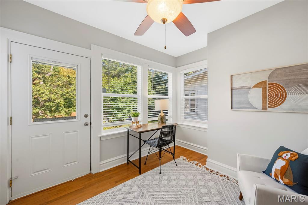 Bright room with a desk by the windows, a white exterior door, and a sofa.