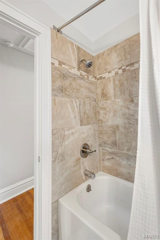Bathroom tub and shower with beige tile and a decorative mosaic border.