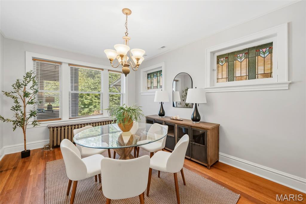 Dining room with a glass-top table, white chairs, stained-glass windows, and hardwood floors.
