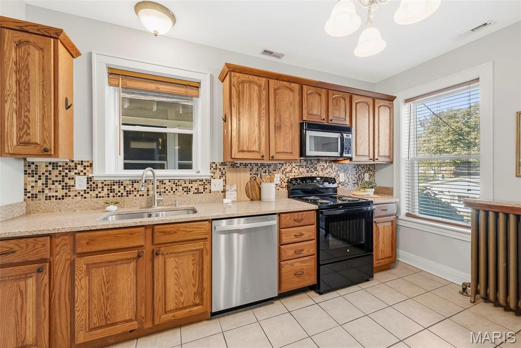Kitchen with oak cabinets, mosaic tile backsplash, stainless-steel dishwasher, and black range.