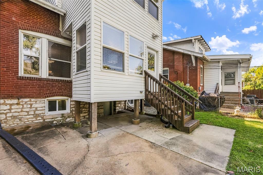 Rear of a brick and white-sided home with a raised addition, wooden stairs, concrete patio, and small lawn.