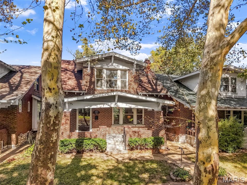 Two-story red-brick house with a covered porch, framed by mature trees.