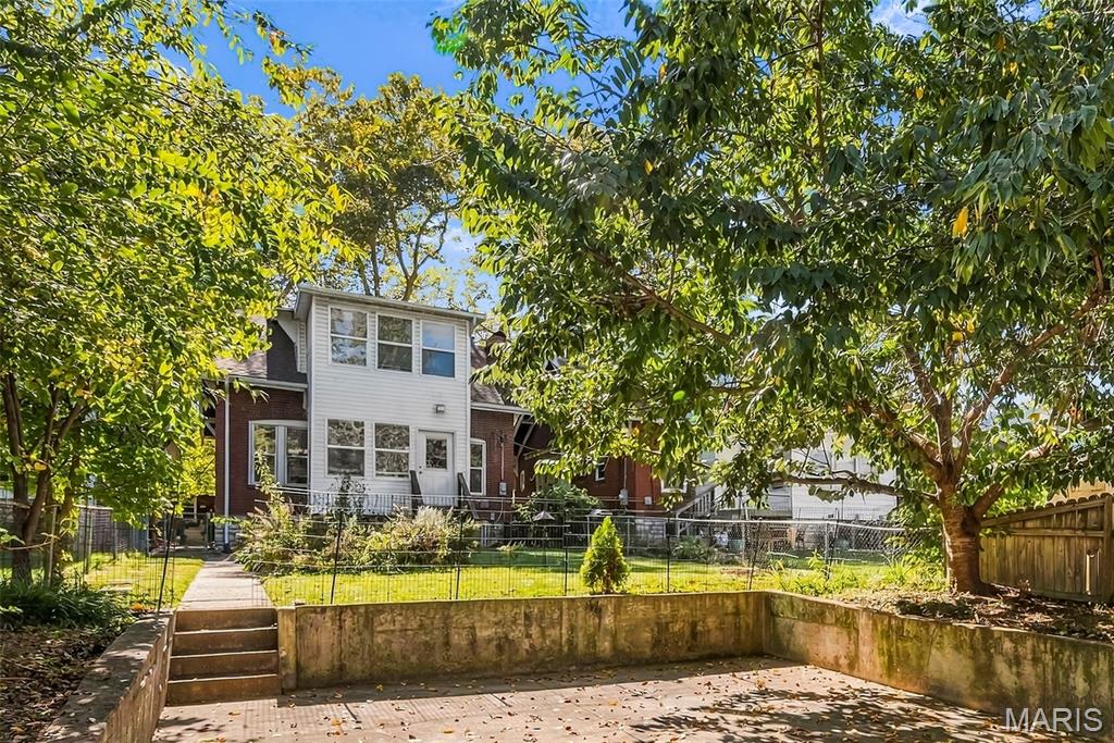 Two-story house behind a fenced yard and sunken patio, shaded by mature trees.
