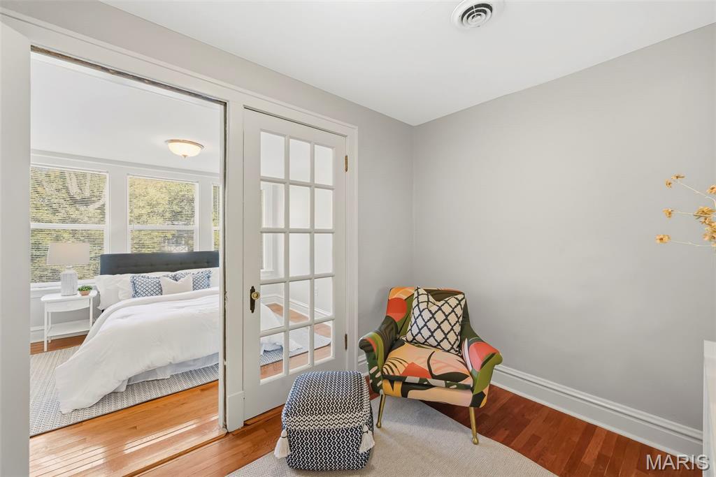 Bedroom with adjoining sitting area, colorful patterned armchair, and glass-paneled French doors.