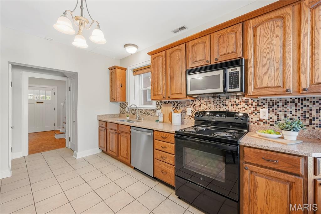 Kitchen with wood cabinets, mosaic tile backsplash, and black range and microwave.