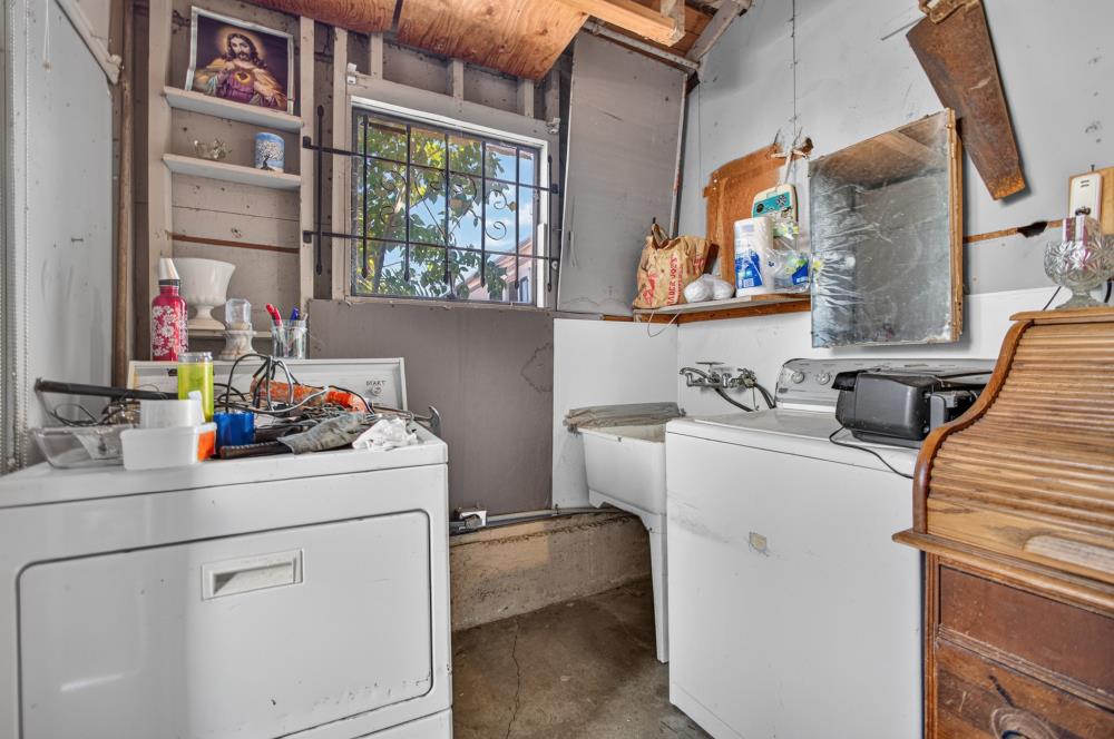 Laundry room with two white washing machines, a utility sink, and a barred window.