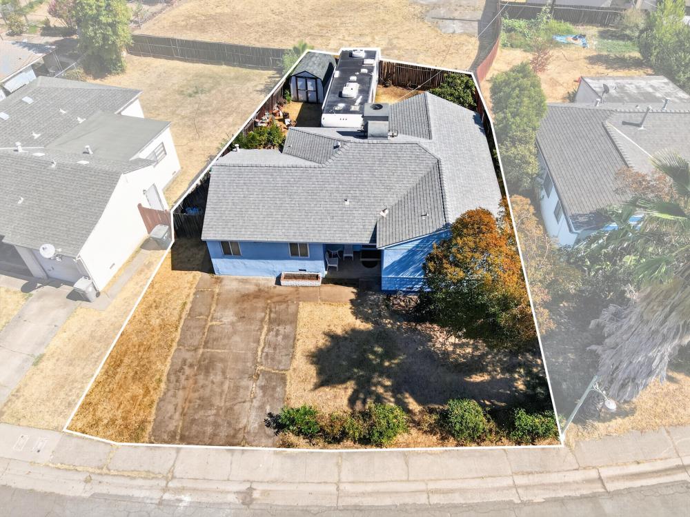 Aerial view of a blue single-story house and dry lot outlined in white, with a paved driveway.