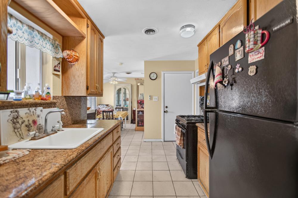 Kitchen with wood cabinets, granite counters, white sink, tiled floor, and black refrigerator.