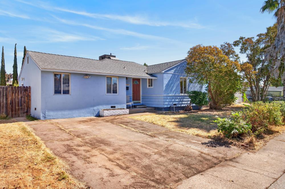 Single-story blue house with a red front door, low porch, and broad concrete driveway.