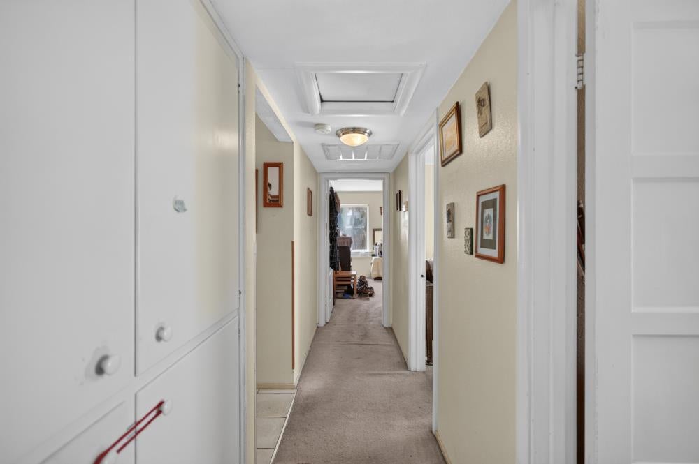 Carpeted hallway with cream walls, framed pictures, and a ceiling light.