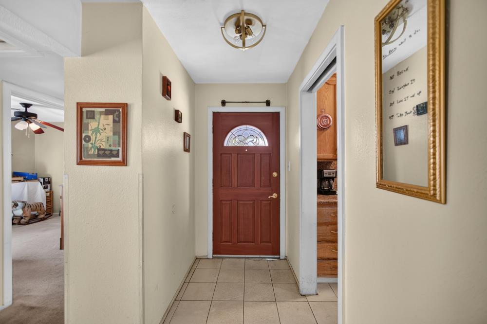 Entry hallway with a reddish-brown front door, tiled floor, framed art, and a large wall mirror.