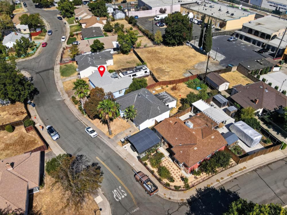 Aerial view of a single-story house with a red map pin, fenced yard, and neighboring properties.
