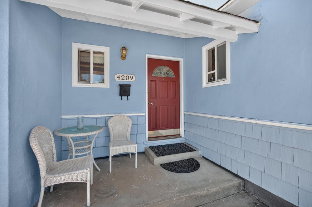 Covered blue front porch with a red door and white wicker seating.