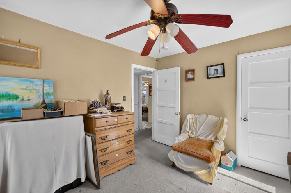 Furnished room with a ceiling fan, wooden dresser, covered furniture, and a draped armchair.