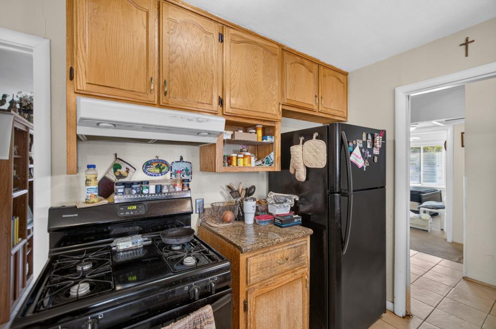 Kitchen with wood cabinets, a black gas range, and refrigerator beside a doorway to a bright room.