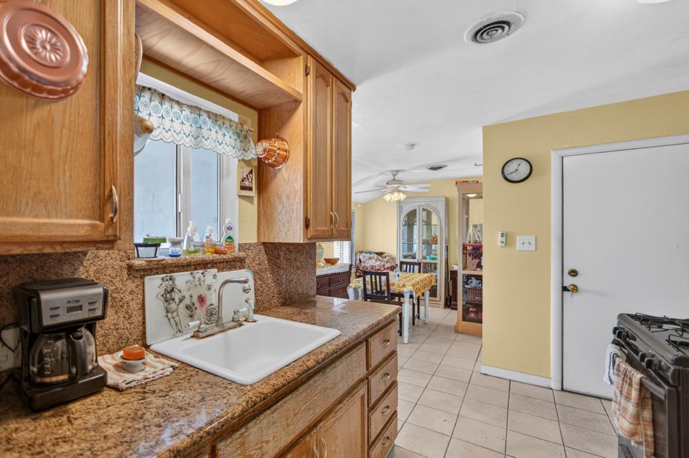 Kitchen with honey-colored wood cabinets, a stone counter, white sink, and adjoining dining area.