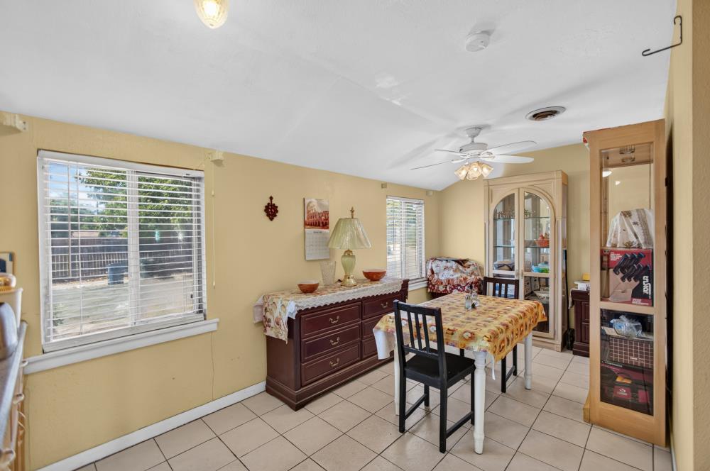 Dining room with a patterned tablecloth, tiled floor, and windows with blinds.