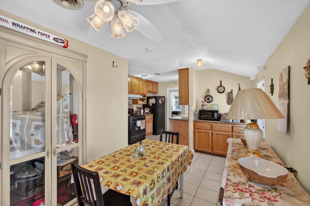 Dining area with a glass-front china cabinet and patterned tablecloth, adjoining a wood-cabinet kitchen.