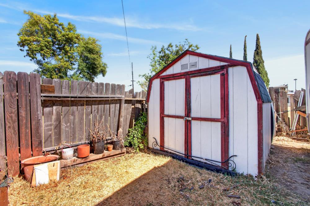 White backyard storage shed with red trim beside a wooden fence and potted plants.