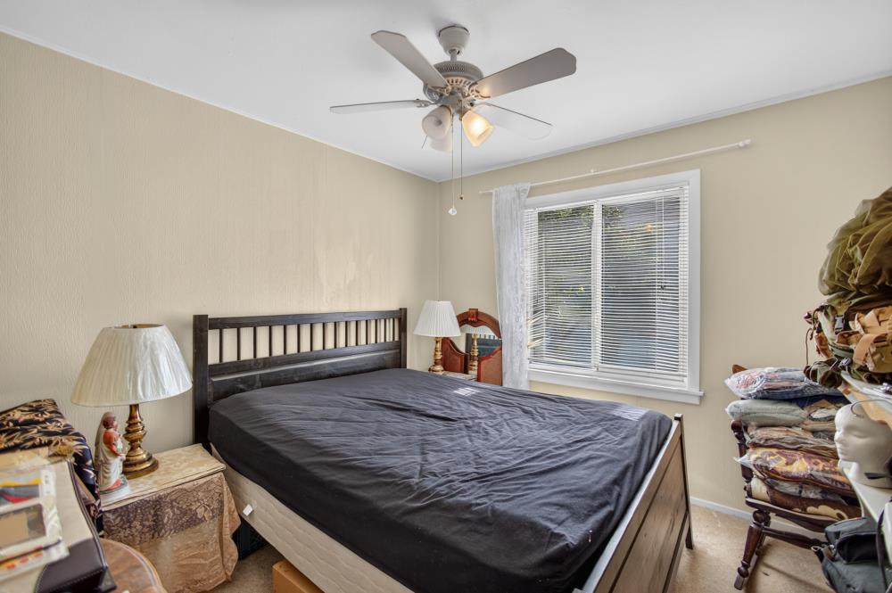 Bedroom with a large bed, dark wood headboard, ceiling fan, and window with blinds.