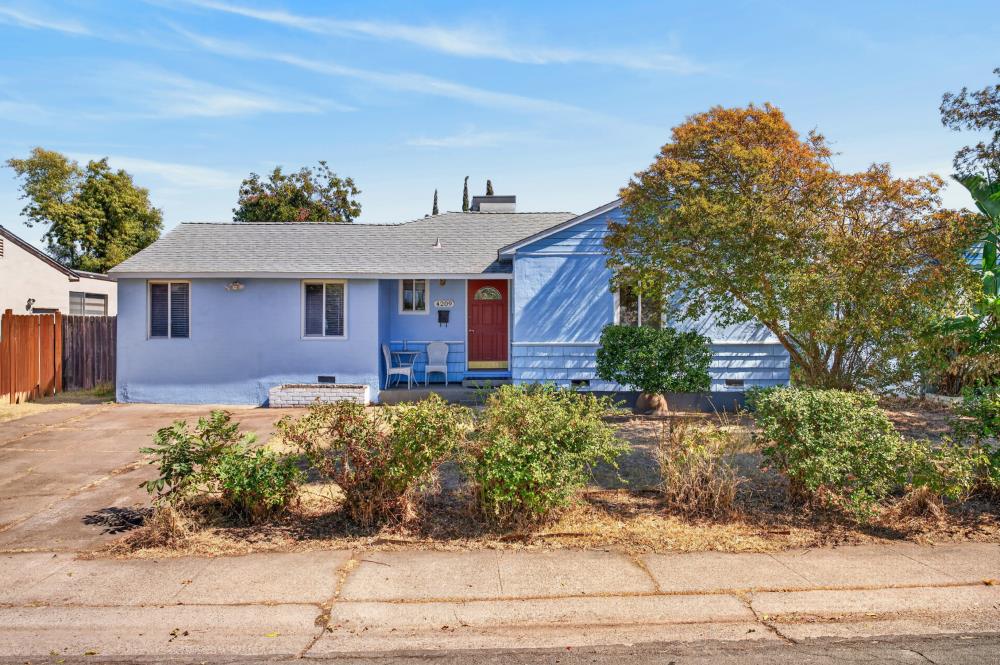 Blue single-story house with a red front door, small porch, and large autumn-colored tree.