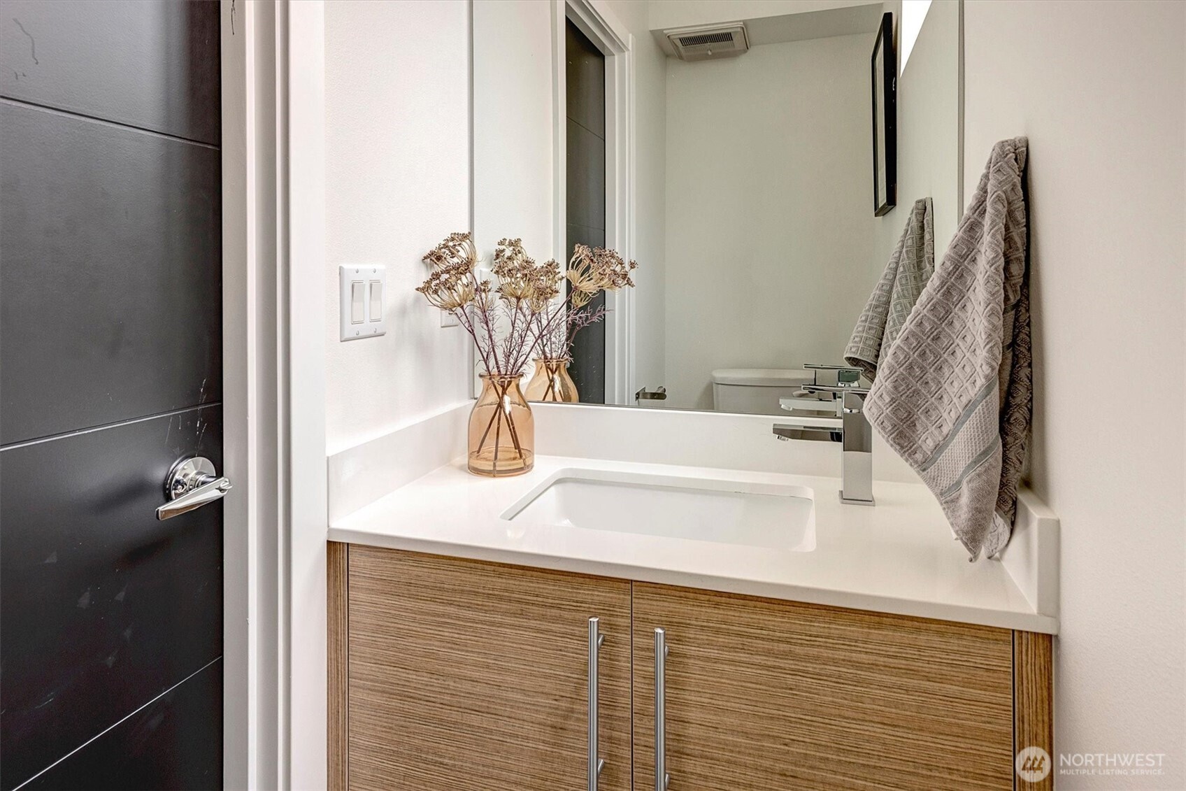 Bathroom vanity with a white sink, wood-grain cabinets, chrome faucet, and gray towels.