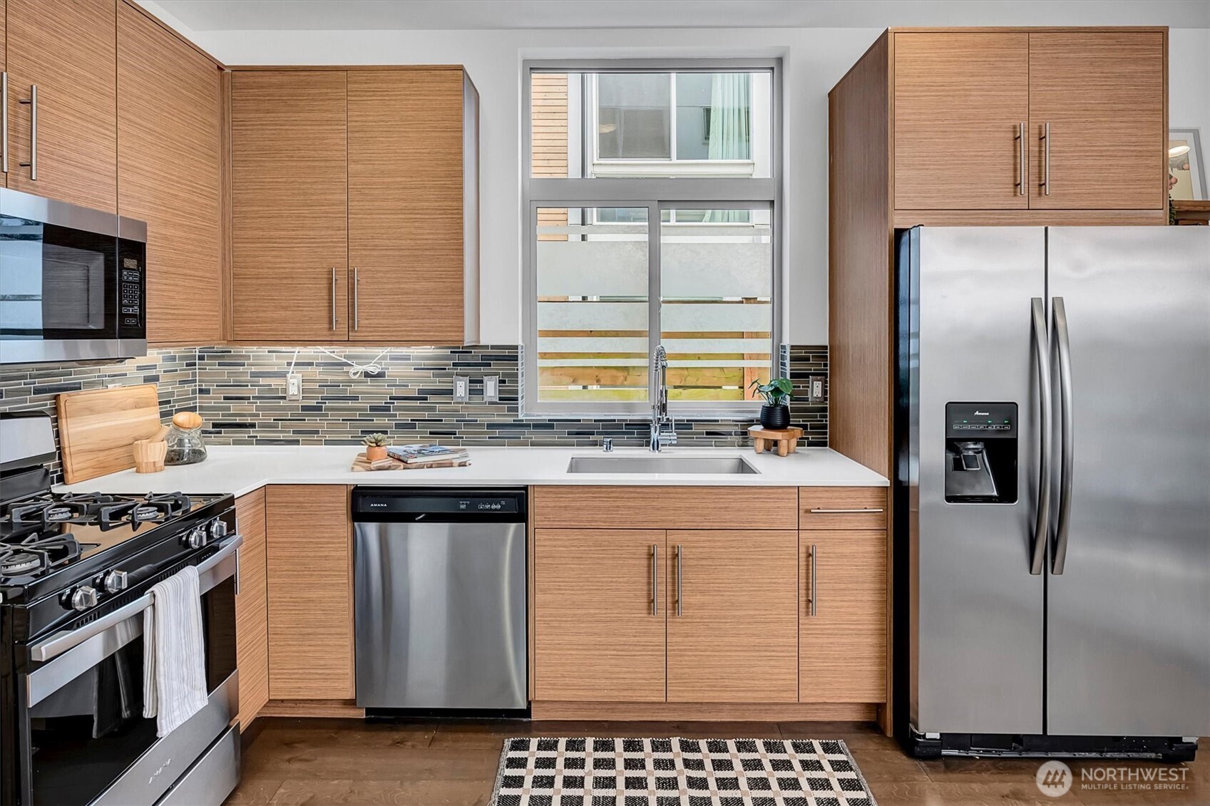Kitchen with wood cabinetry, stainless steel appliances, mosaic backsplash, and a window over the sink.