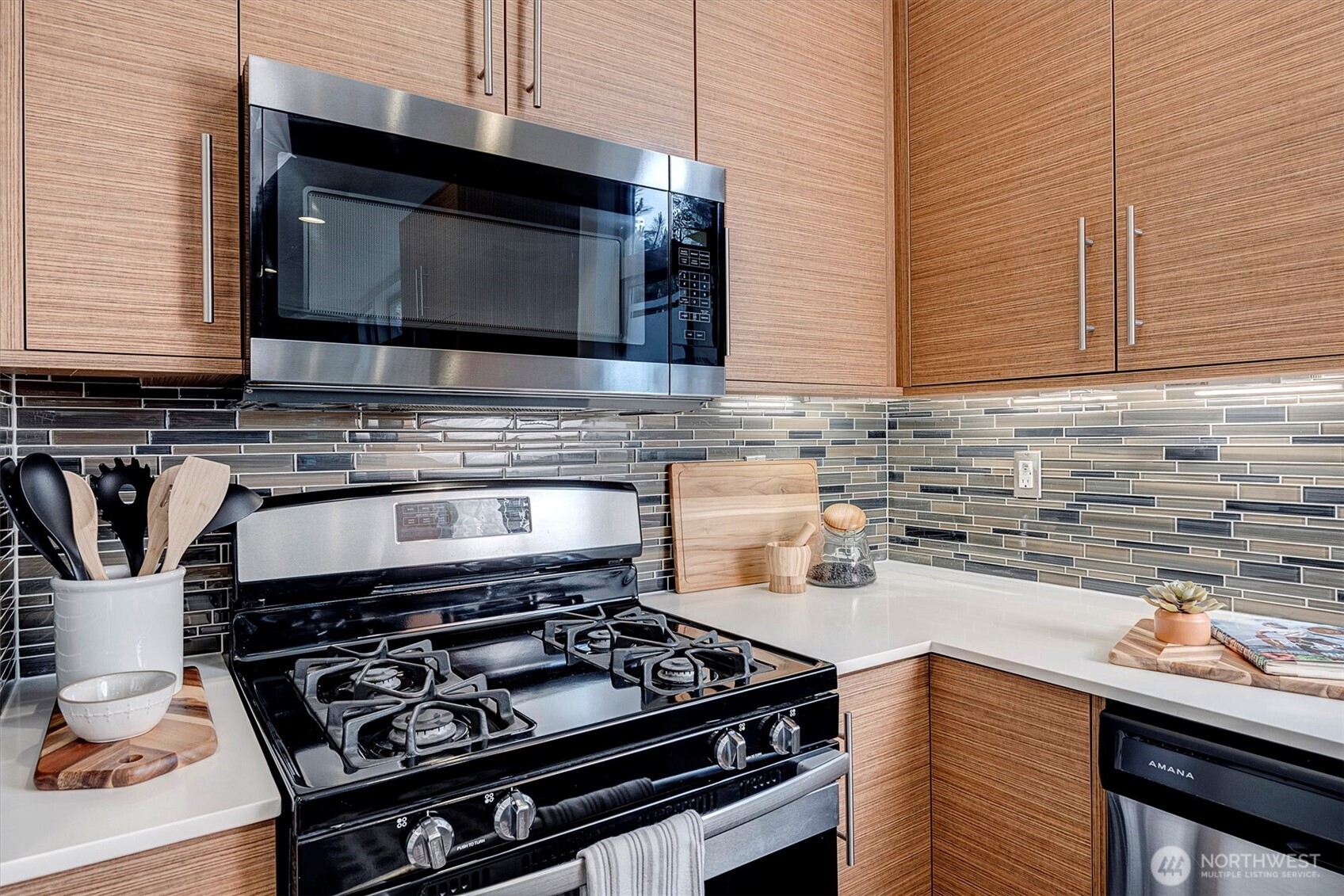 Kitchen with wood cabinets, a black gas range, stainless microwave, and multicolored tile backsplash.