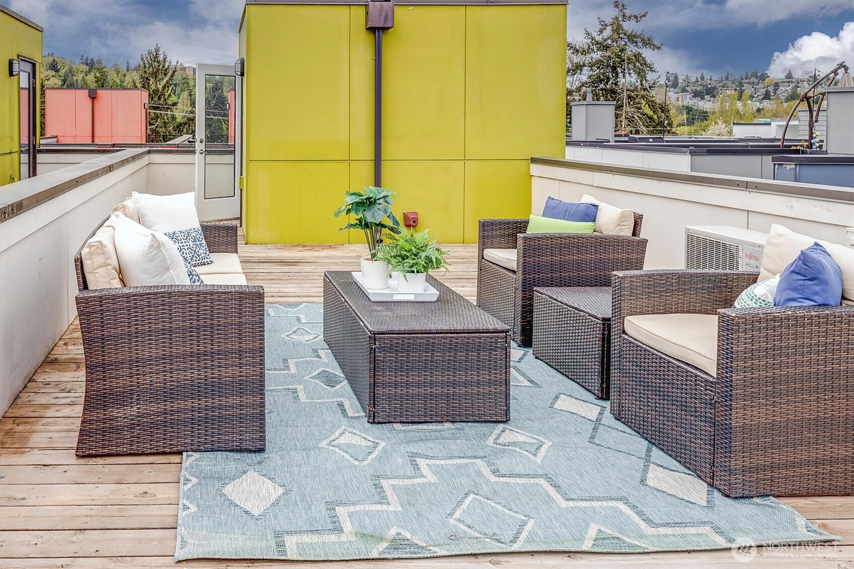 Rooftop deck with woven lounge seating, a geometric rug, and a bright yellow wall.